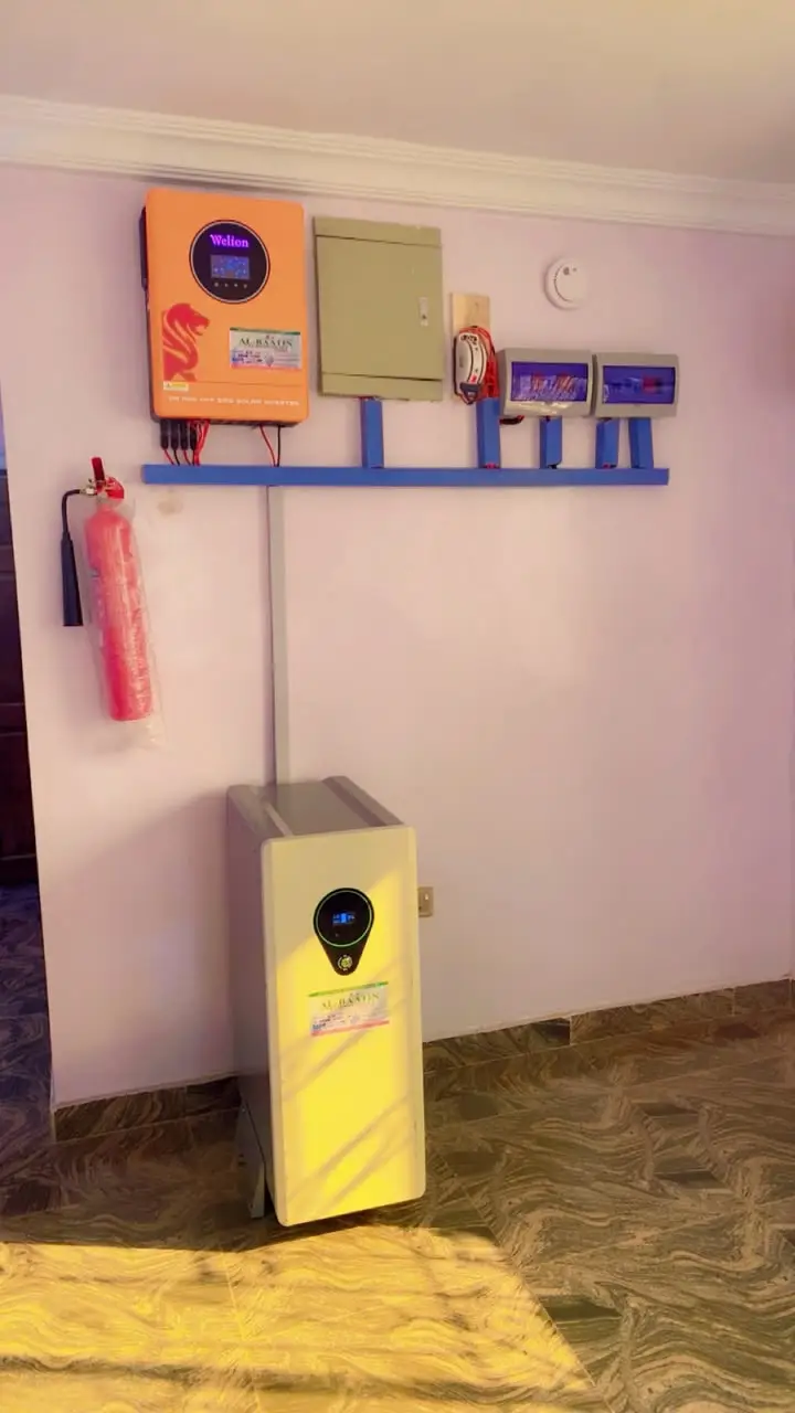 An orange Welion hybrid inverter mounted on a rail beside the distribution box and breakers, with a floor-standing lithium battery below and a fire extinguisher on the wall.