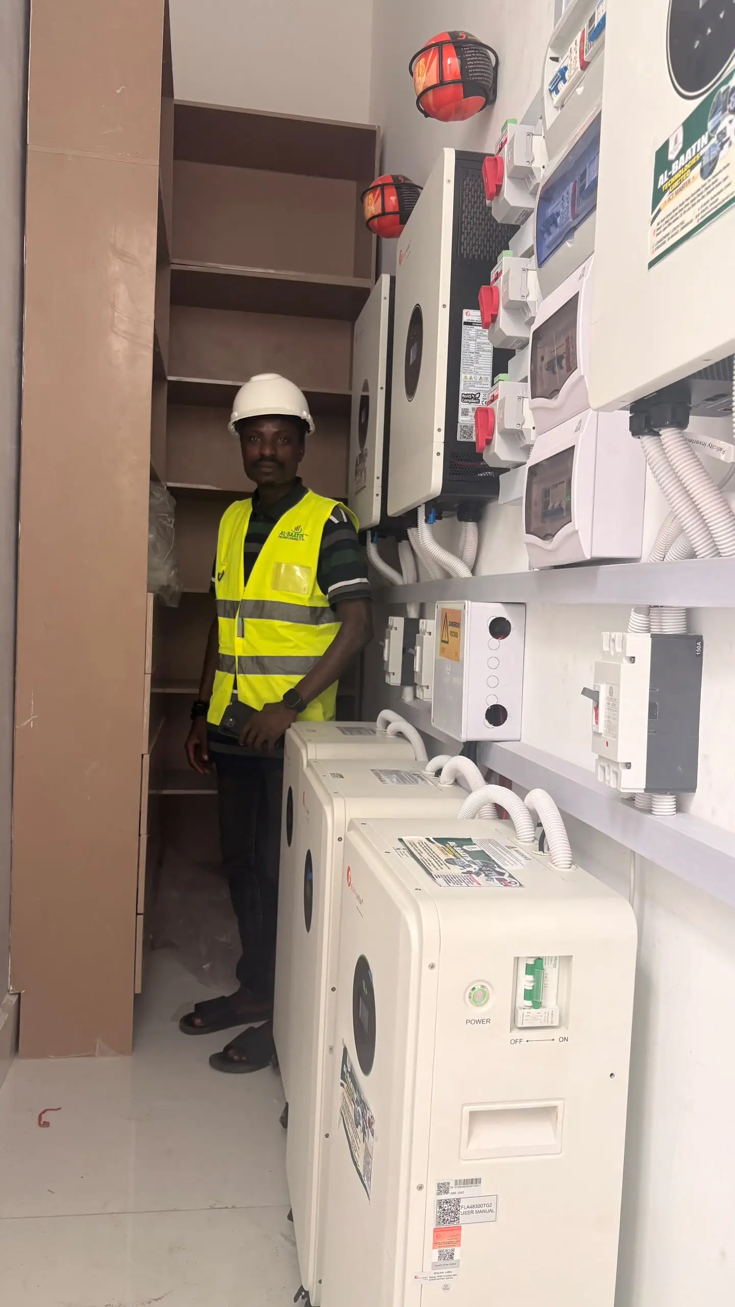 An Al-Baatin fitter standing beside the finished inverter and battery wall.