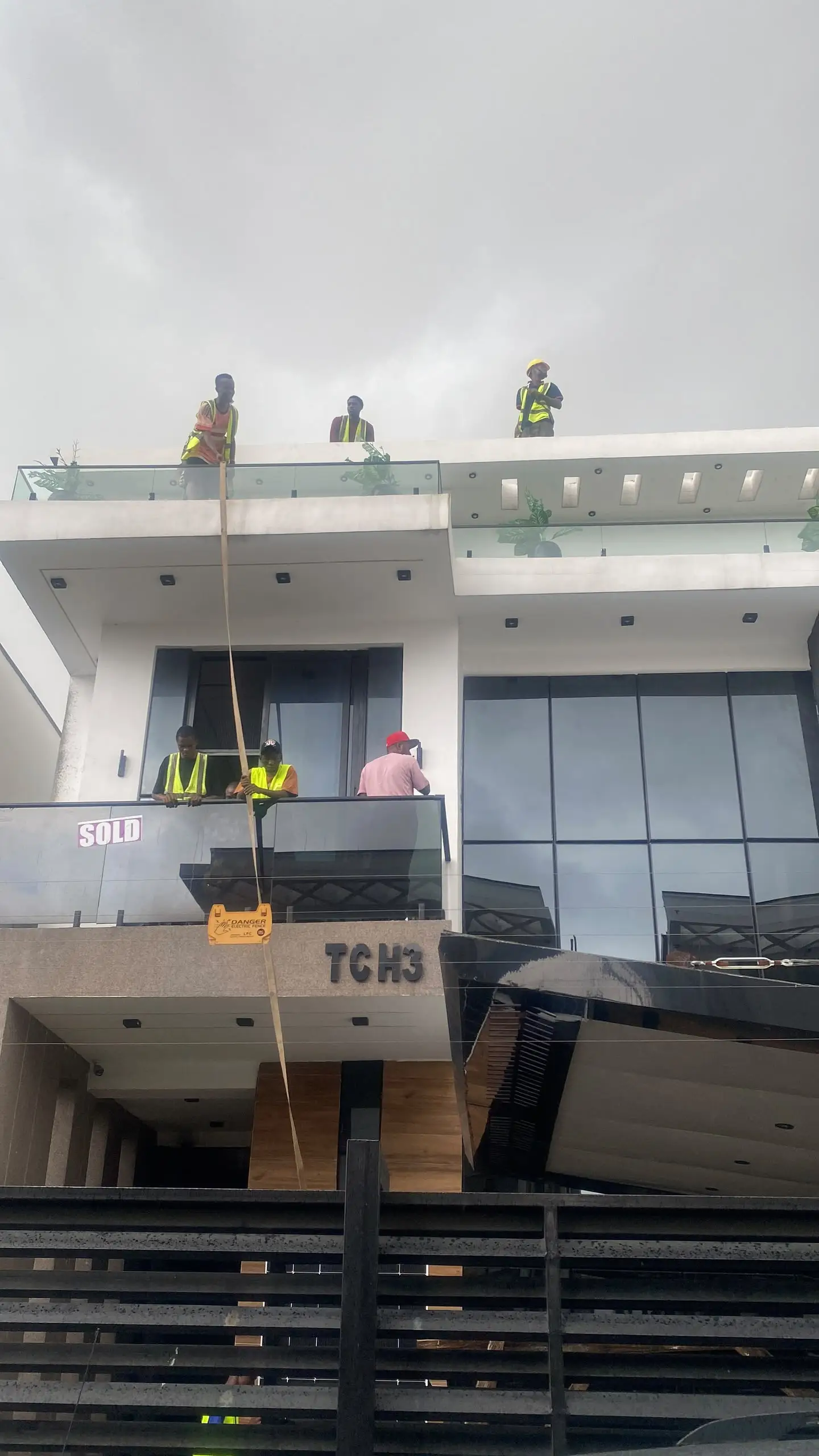 Al-Baatin fitters in hi-vis vests hoisting a solar panel up to the roof from the balcony below.