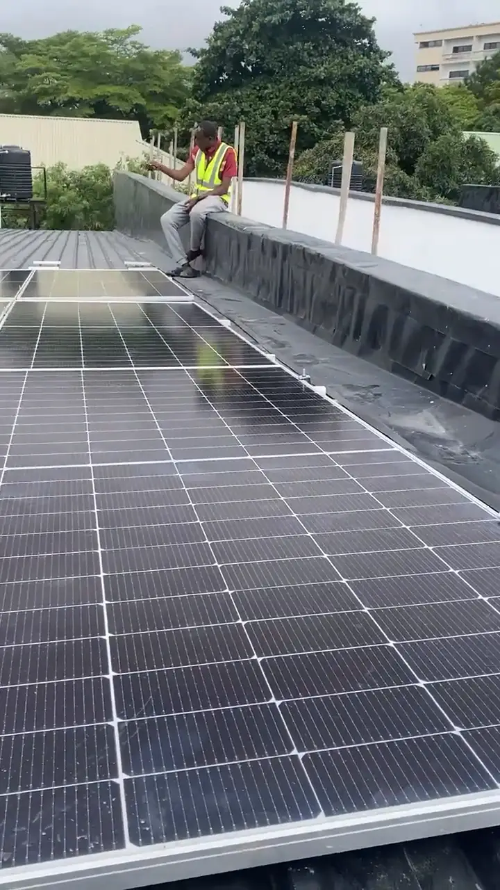 A pan across the installed rooftop array, a fitter in a hi-vis vest sitting on the parapet behind it.