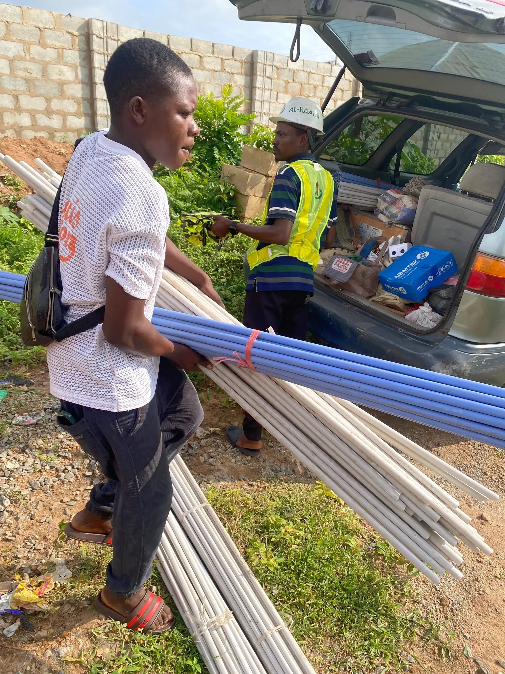 The crew carrying lengths of conduit pipe into the building.